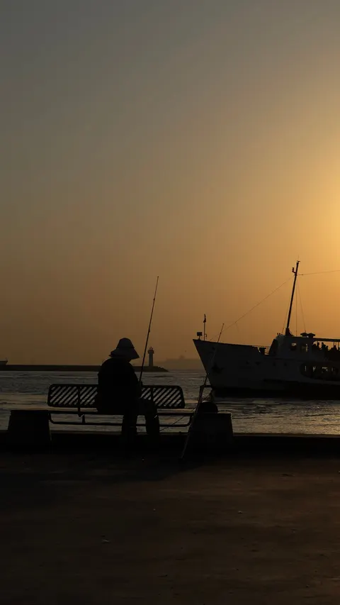 A figure on a bench at sunset, a ferry passing behind
